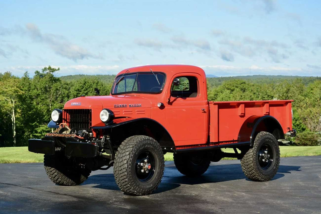 Restored red 1950 Dodge Power Wagon with off-road tires parked on a blacktop with trees and hills in the background