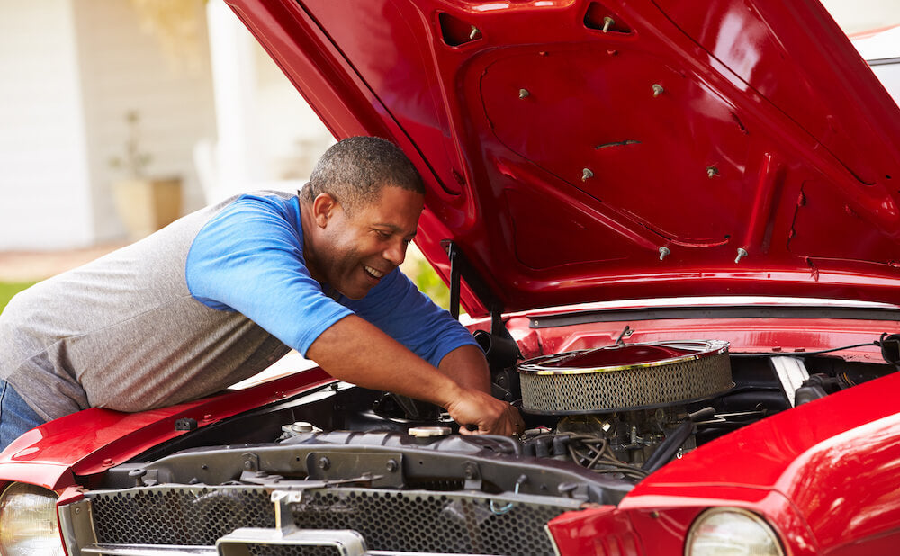 Man working on classic car parked in a garage with its hood open