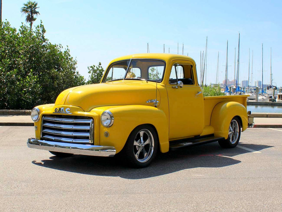 Bright yellow 1951 GMC 5-window pickup parked near a marina with chrome wheels and a restored body